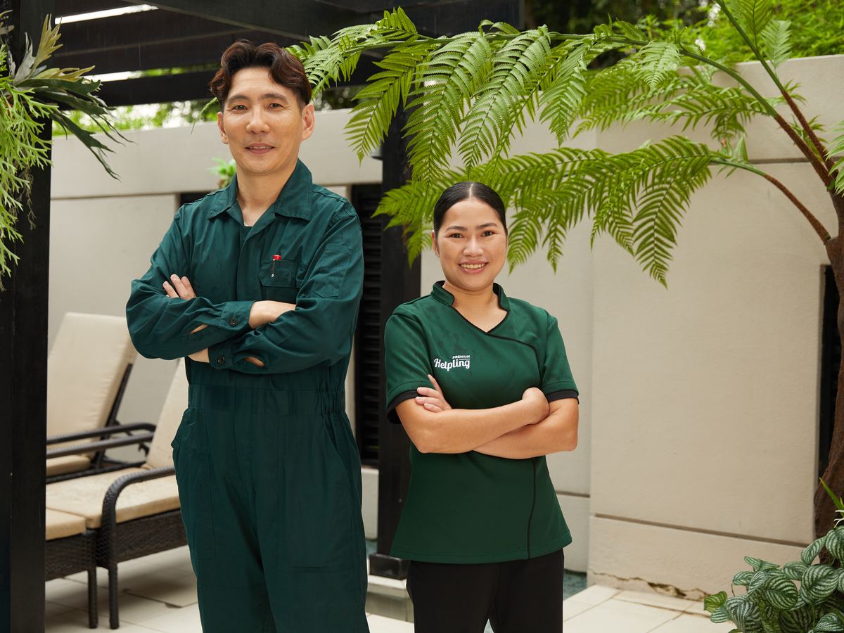 Two certified Helpling professionals in green uniforms standing confidently in a garden patio